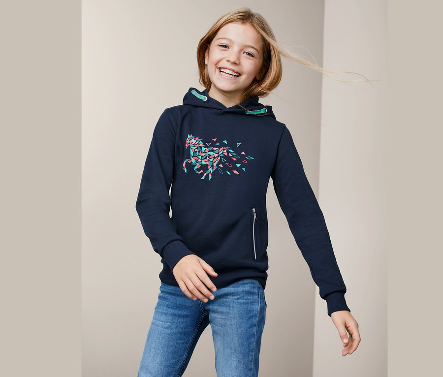 Usmívající se dívka má na sobě tmavě modrou mikinu s kapucí a potiskem koně a džíny.