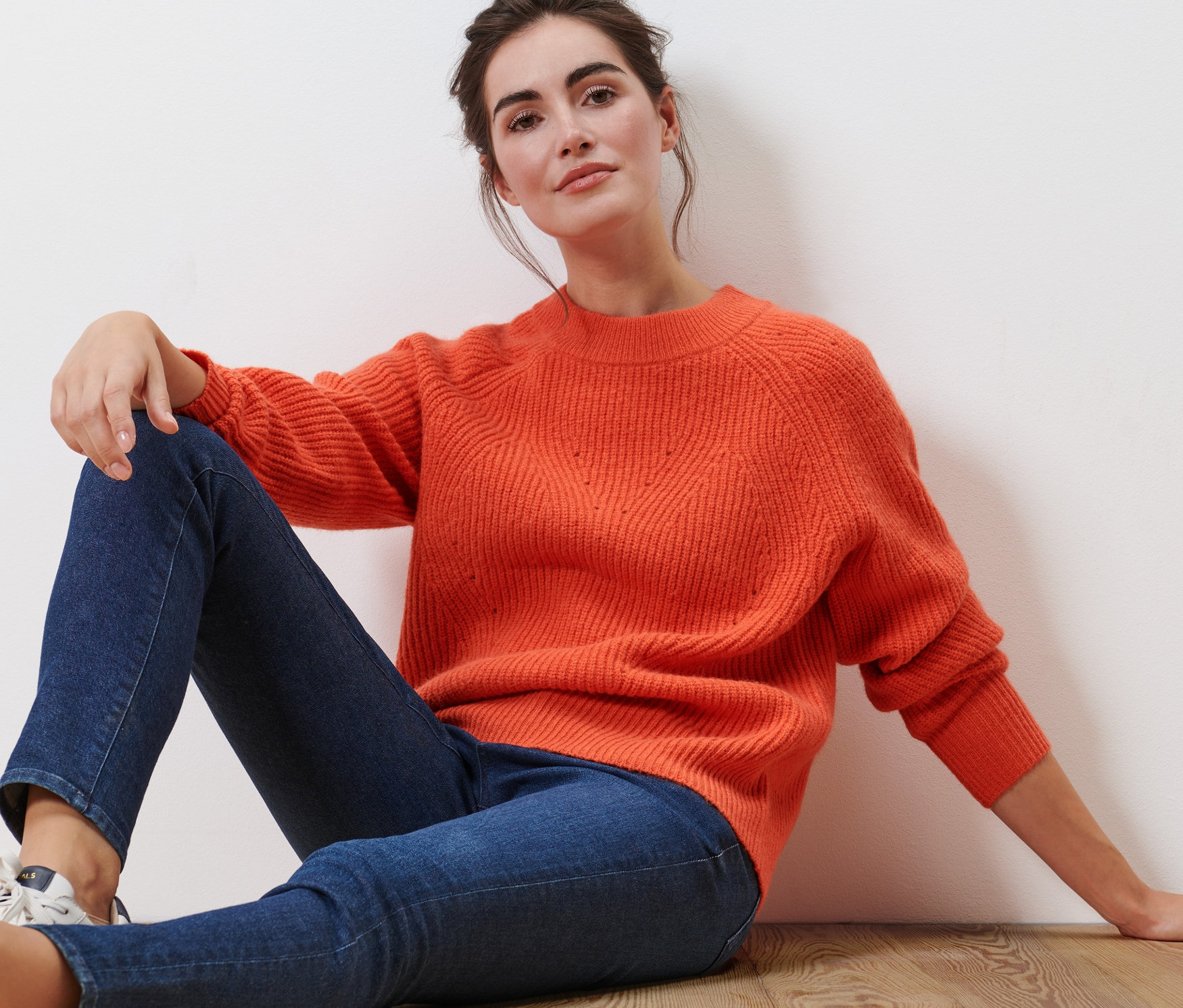 Žena sedí na podlaze a má na sobě oranžový pletený svetr.