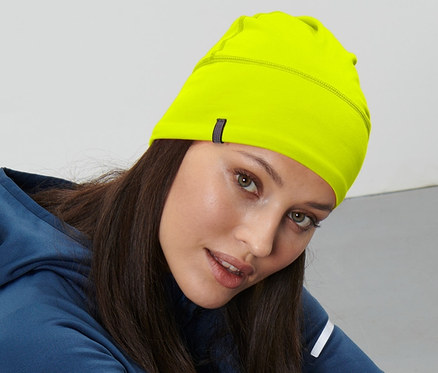 Žena sedí na zemi a má na sobě neonově žlutou termo čepici.