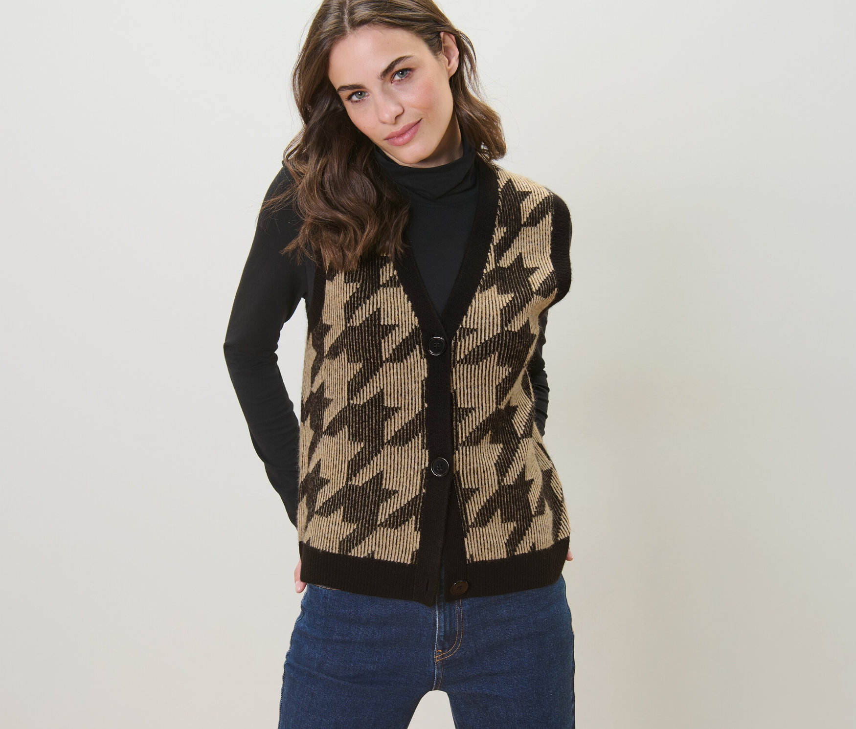 Žena pózuje v pletené vestě se žakárovým vzorem kohoutí stopy.