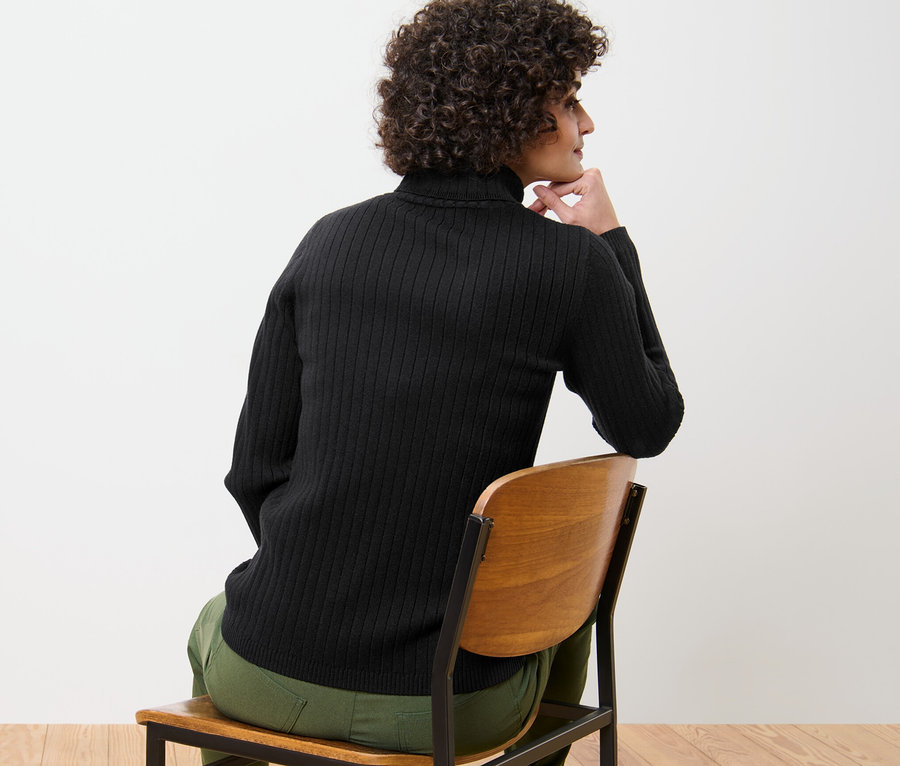 Žena sedí na židli a má na sobě černý žebrovaný rolák.