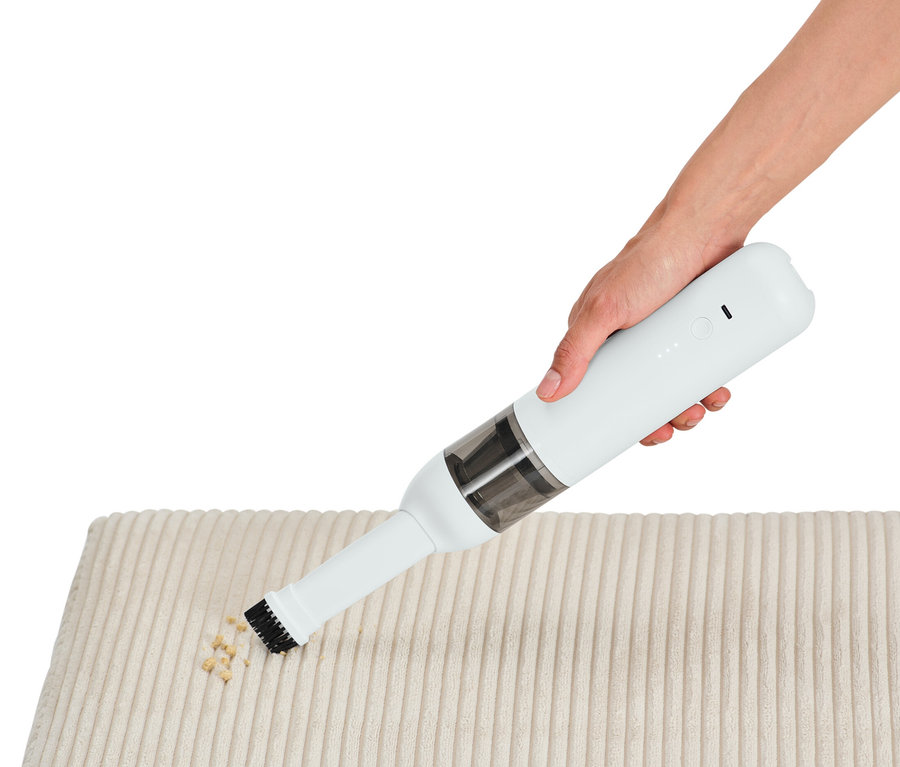 Ruka používá akumulátorový ruční vysavač na čištění krémové látky od drobků.