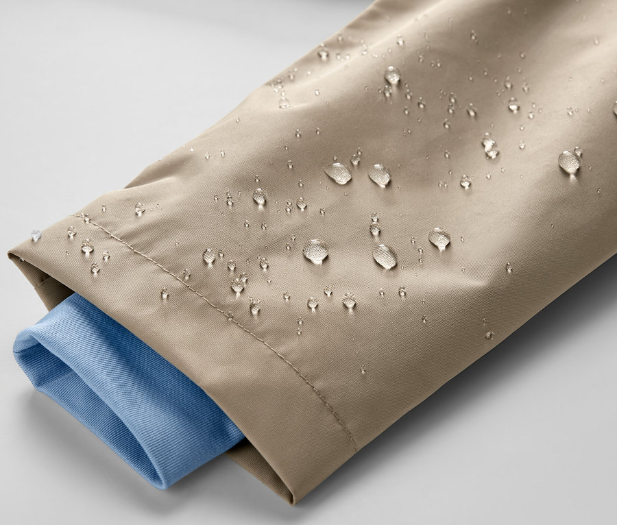 Detail dětské hnědé bundy do deště s kapkami vody a modrým rukávem košile.