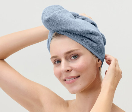Žena si upravuje světle modrý ručníkový turban na hlavě.