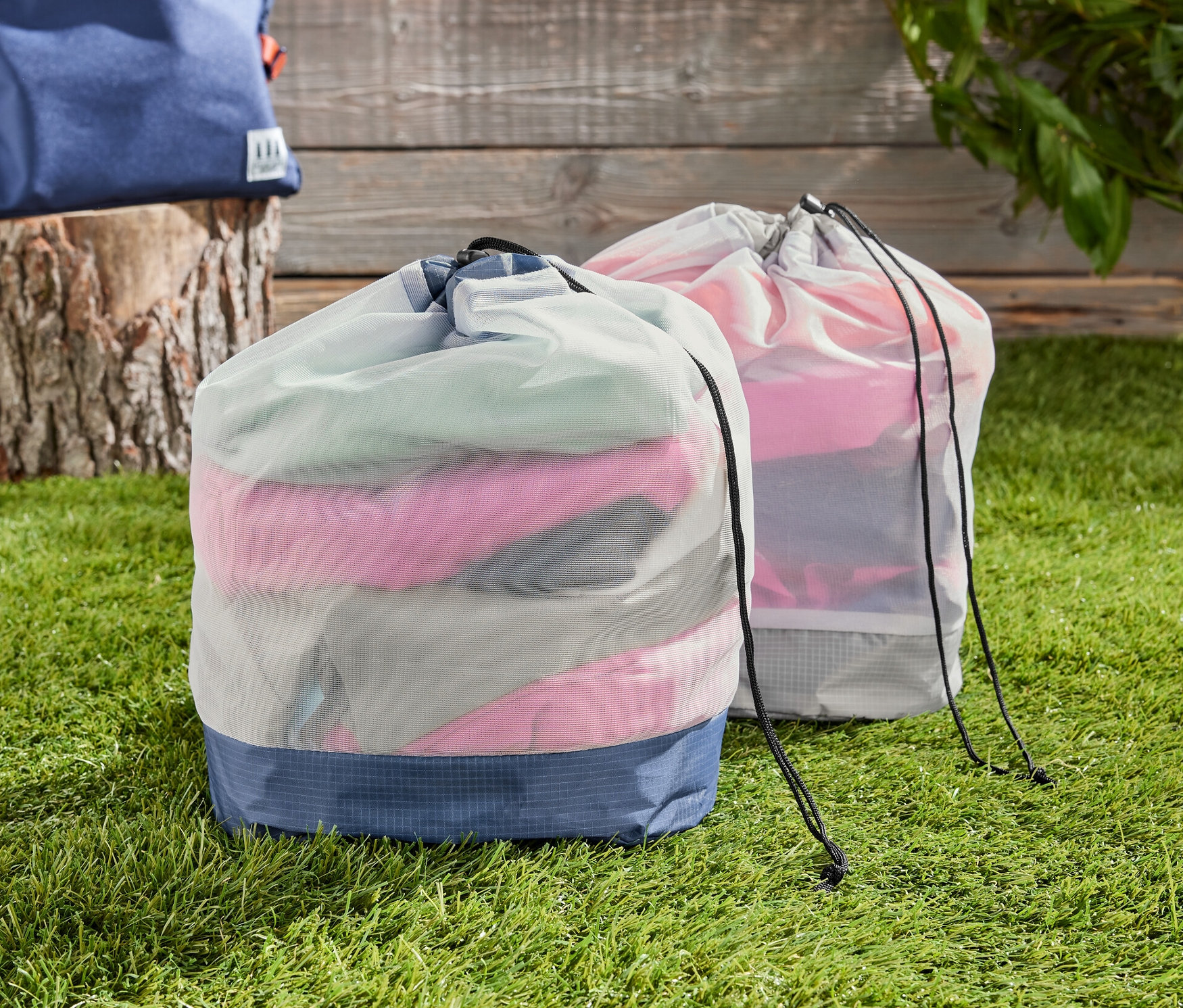 Dva outdoorové síťované sáčky na trávě, v pozadí batoh.