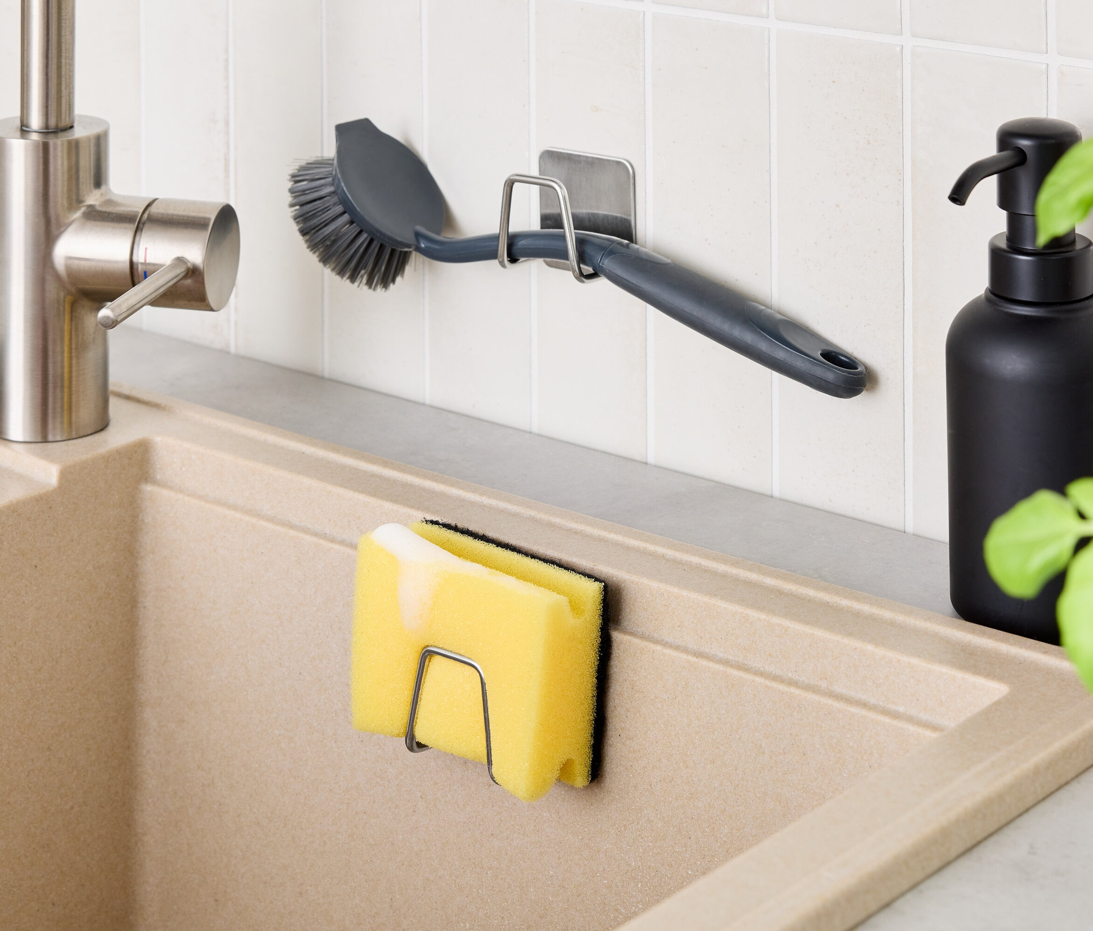 V kuchyni je béžový dřez s baterií. Na zdi je držák s kartáčem a na dřezu držák s houbičkou. Vedle dřezu je černá láhev.