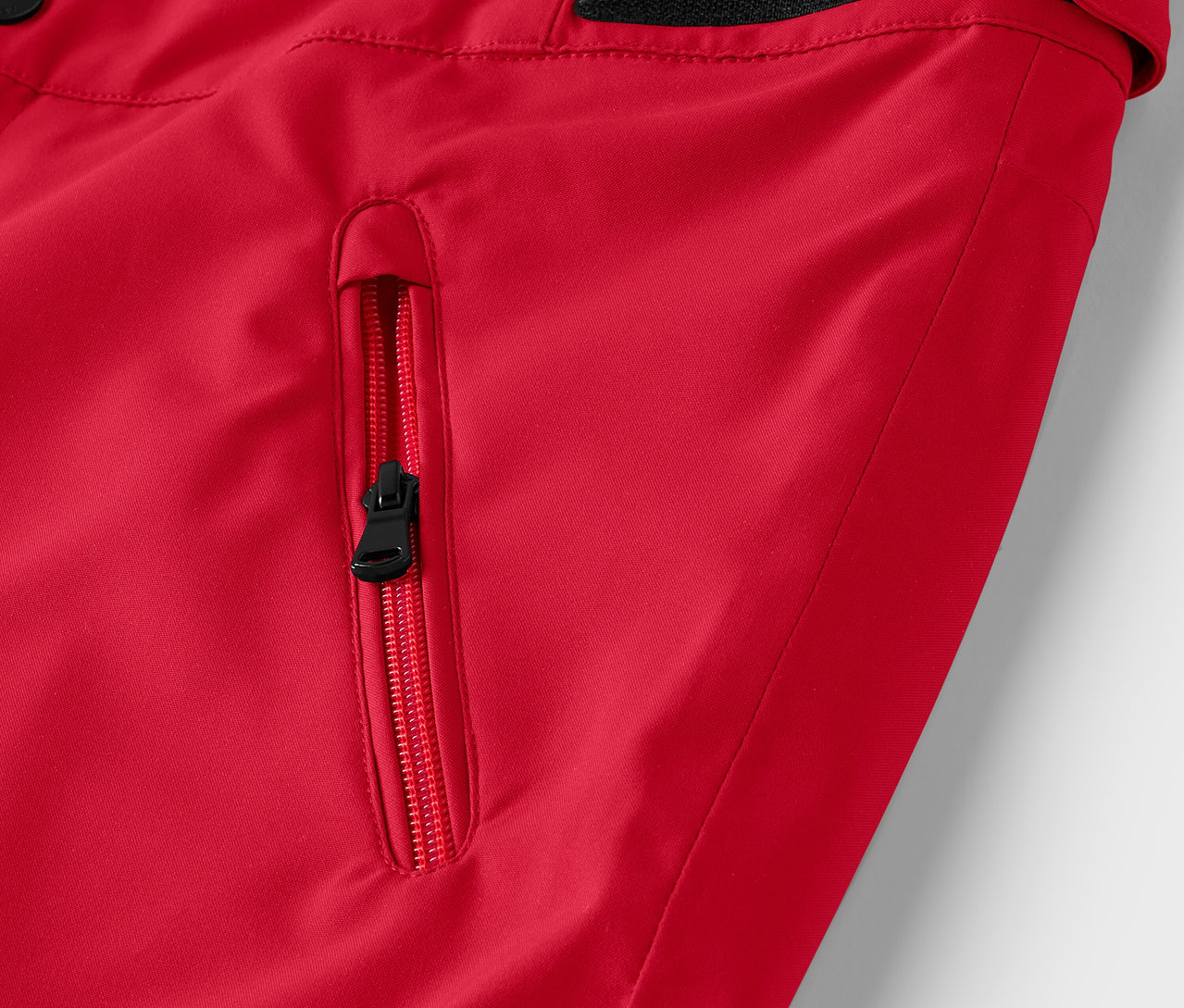 Detail červené bundy s černým zipem na kapse.
