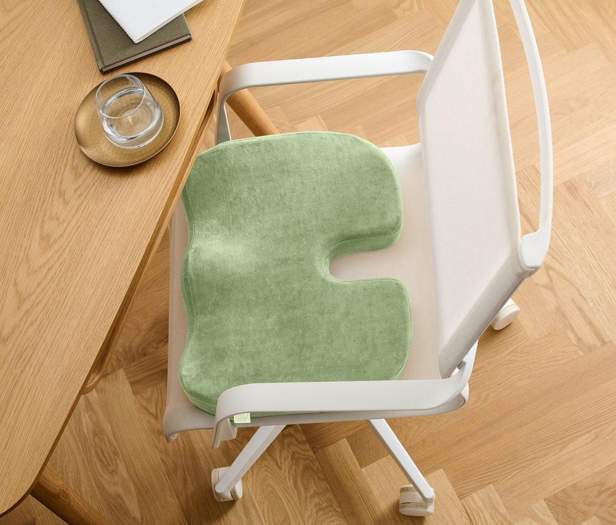 Zelený sedák na židli s výřezem ve tvaru písmene U. Židle stojí u dřevěného stolu.