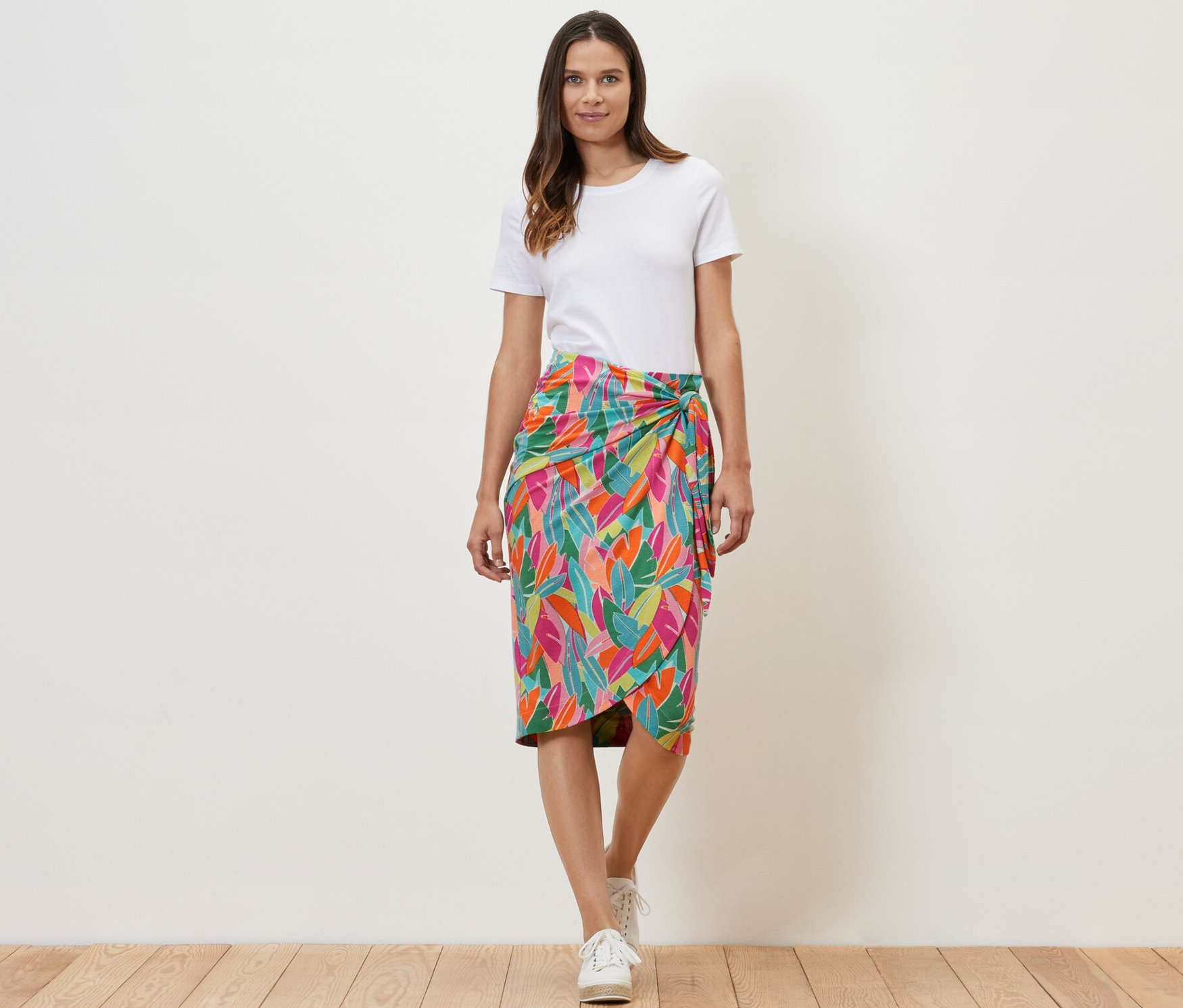 Žena stojí a má na sobě zavinovací žerzejovou sukni s potiskem listů.