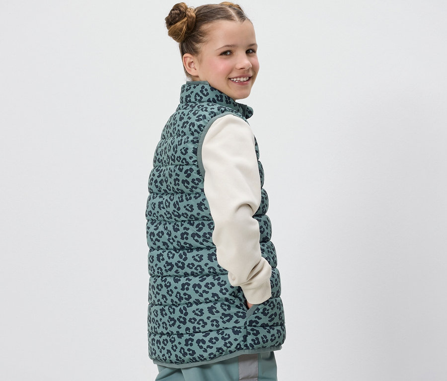 Dívka se usmívá přes rameno a má na sobě prošívanou vestu Kinder s leopardím potiskem.
