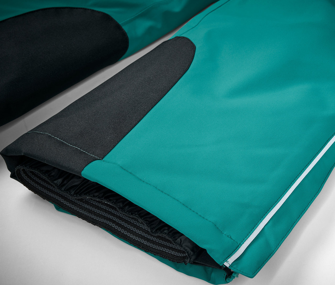 Detailní záběr na smaragdově zelené lyžařské kalhoty s černými detaily a bílým pruhem.