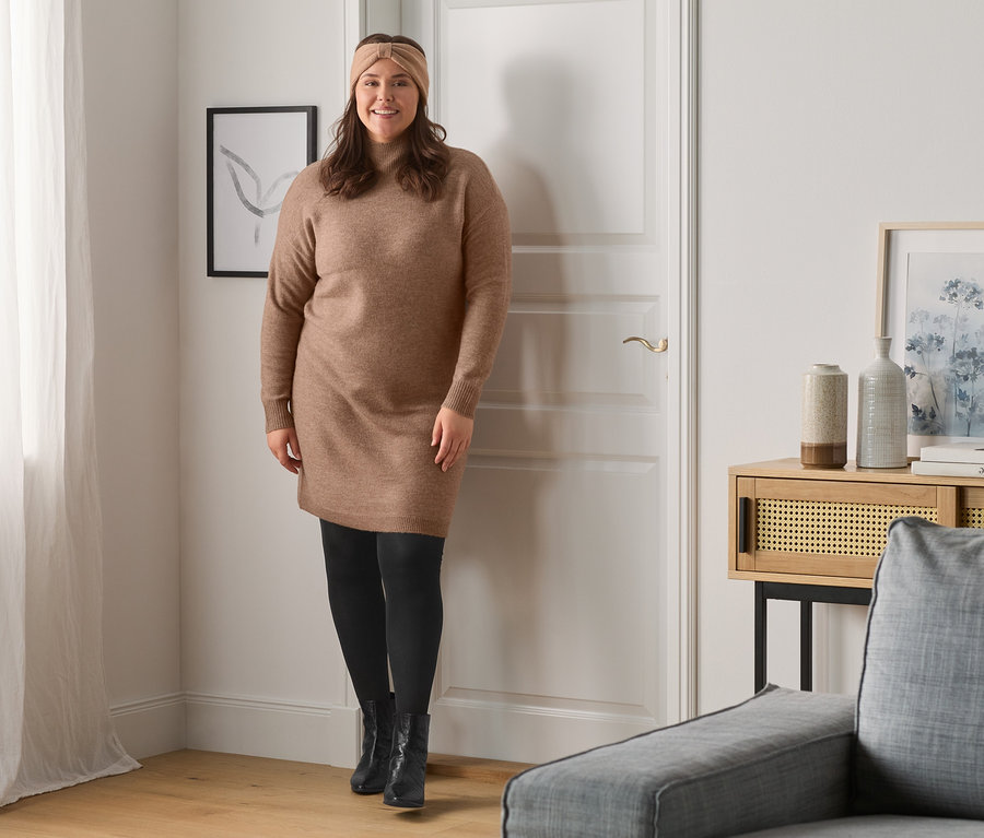 Žena pózuje v pletených šatech a černé obuvi.