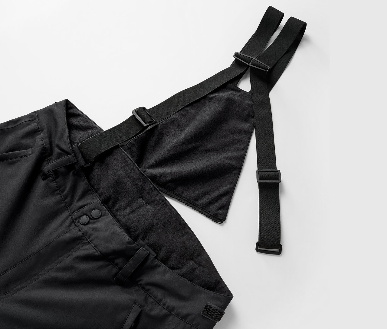 Detailní pohled na černé kalhoty s laclem a nastavitelnými popruhy.
