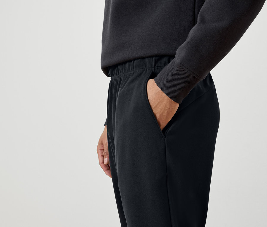 Muž má ruku v kapse černých tepláků.