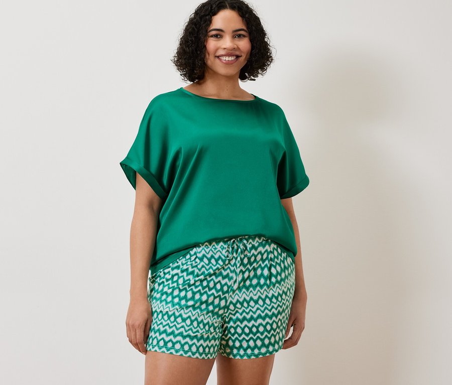 Žena má na sobě zelenomodré tričko z kombinace materiálů a dvoje žerzejové šortky.