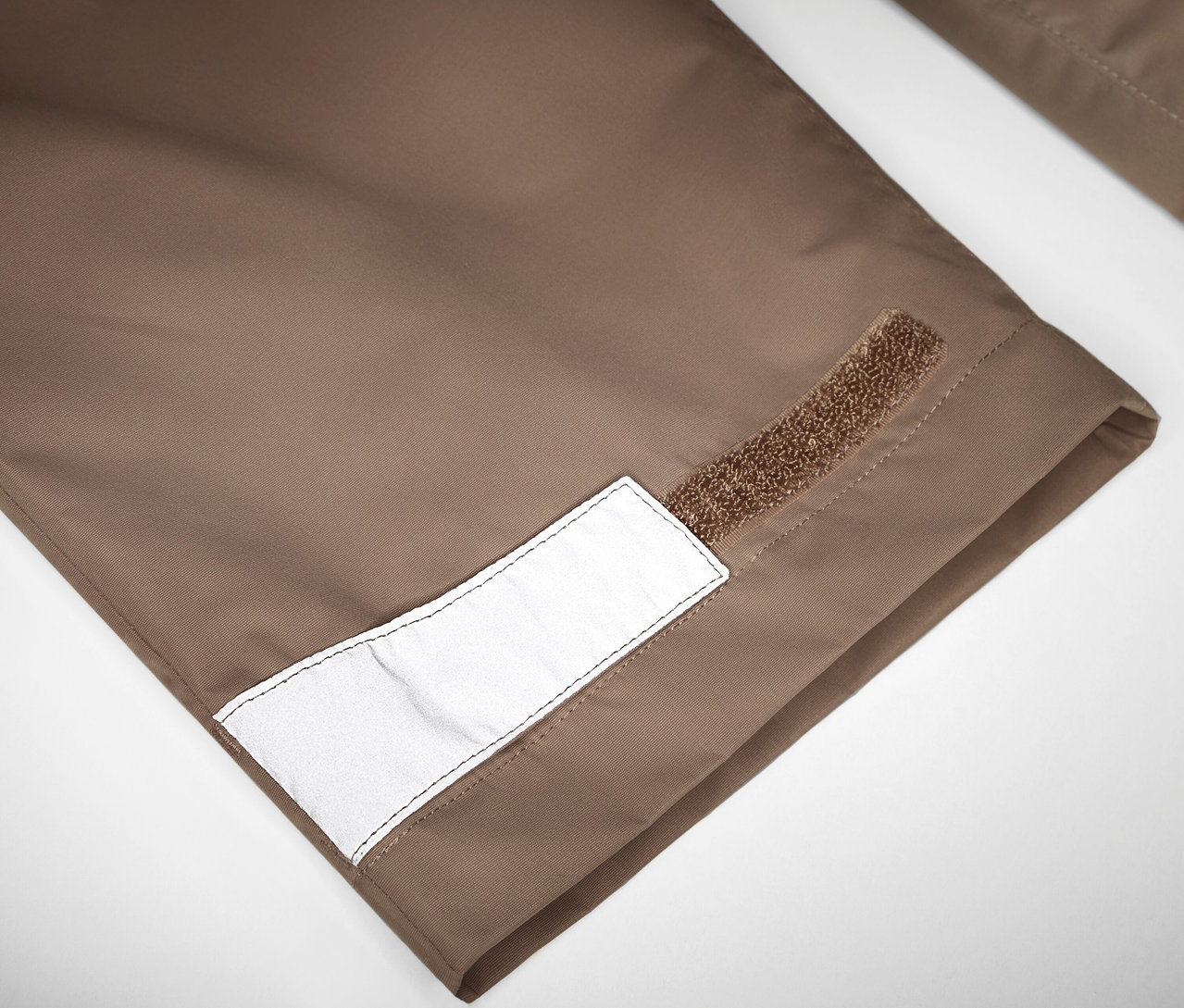 Detail dětských kalhot do deště s reflexním prvkem a suchým zipem.