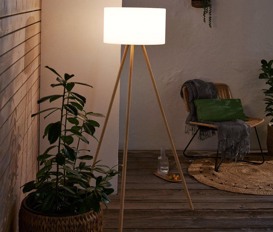 Interiér s LED akumulátorovou stojací lampou v dřevěném vzhledu, která stojí vedle rostliny v proutěném koši.