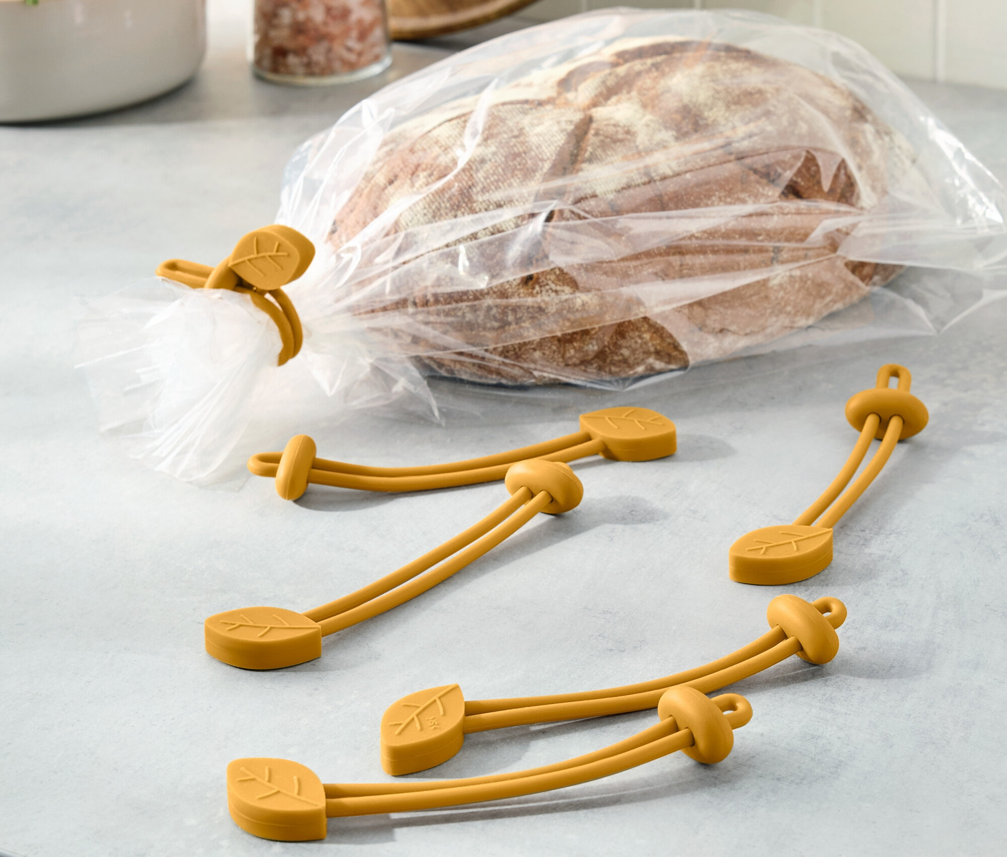 Chléb v igelitovém sáčku je uzavřený žlutou gumičkou s motivem listu. Další tři gumičky leží vedle.