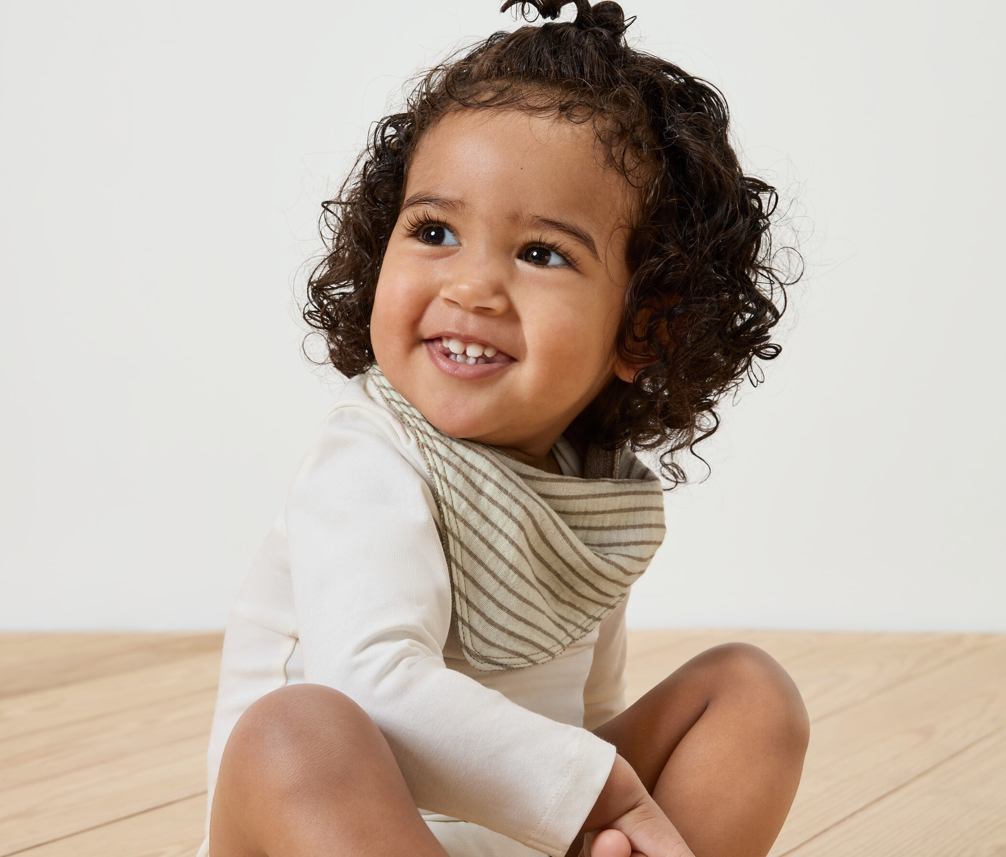 Usmívající se dítě sedí na dřevěné podlaze a má na sobě mušelínový šátek na krk, 5 ks.