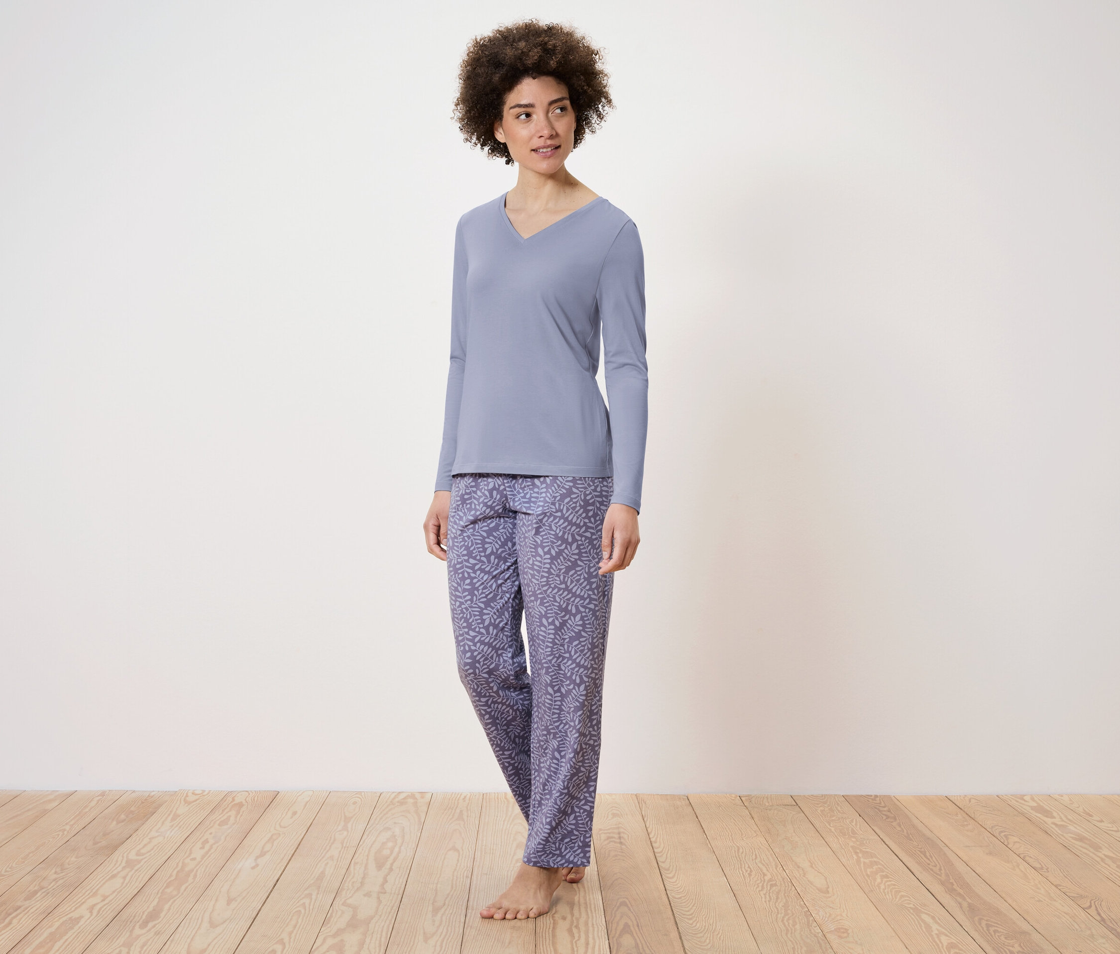 Žena stojí a má na sobě modré pyžamo s dlouhým rukávem a vzorované kalhoty.