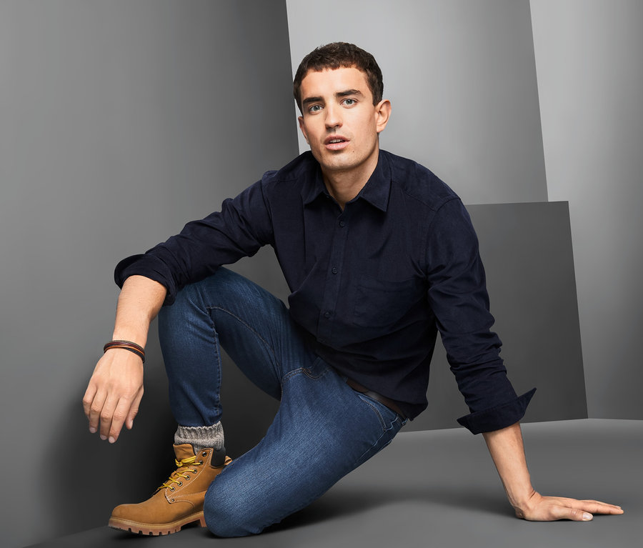 Muž v modré manšestrové košili klečí na zemi.