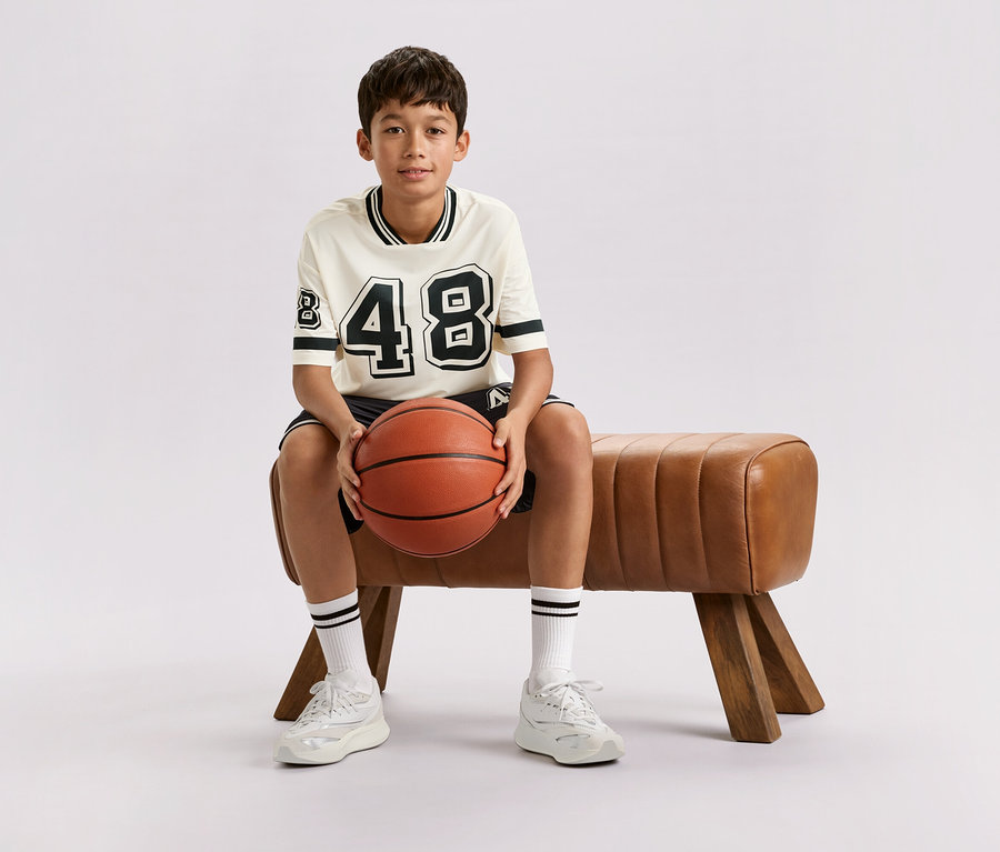 Chlapec sedí na hnědé lavičce a drží basketbalový míč.