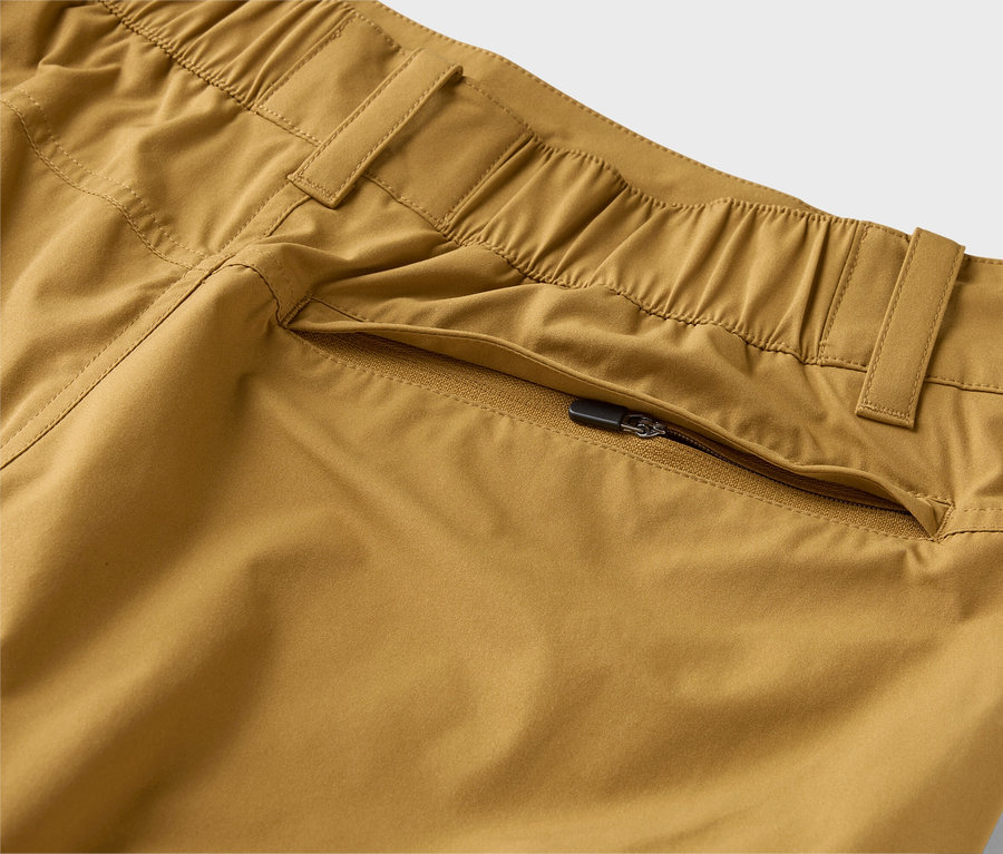 Detailní záběr khaki kalhot s elastickým pasem a kapsou na zip.