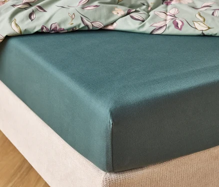 Detailní záběr na tmavě zelenou matraci s mátově zeleným prostěradlem s květinovým vzorem nahoře.