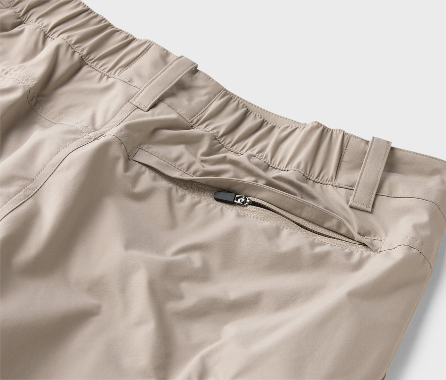 Detail béžových kalhot s elastickým pasem a kapsou na zip.