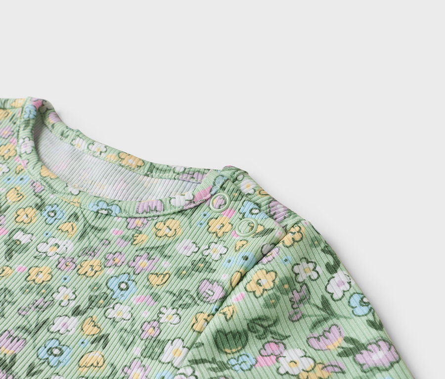 Detailní záběr na světle zelené dětské body s květinovým vzorem a patentkami na rameni.