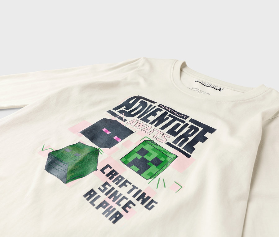 Na bílé košili s dlouhým rukávem je design Minecraft s nápisem "Adventure Awaits" a "Crafting Since Alpha".