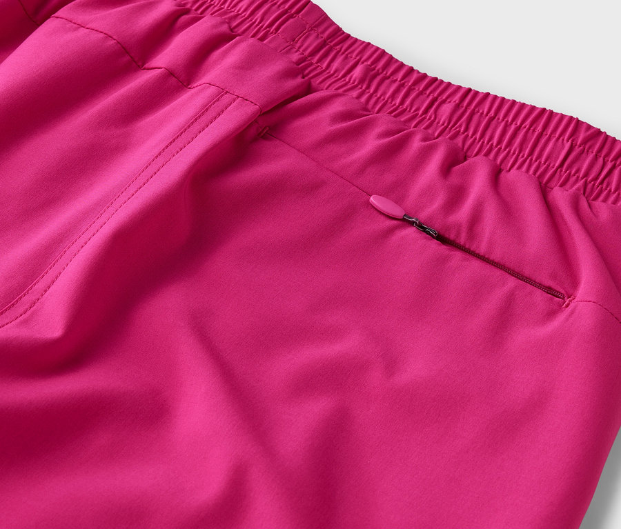 Detailní záběr na růžové kalhoty s elastickým pasem a kapsou na zip.