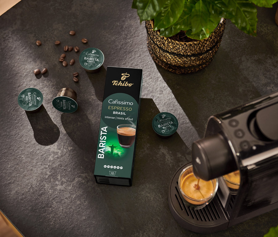 Espresso kávovar plní šálek. V pozadí je balení kapslí Espresso Brasil – 10 kapslí a kávové zrno.