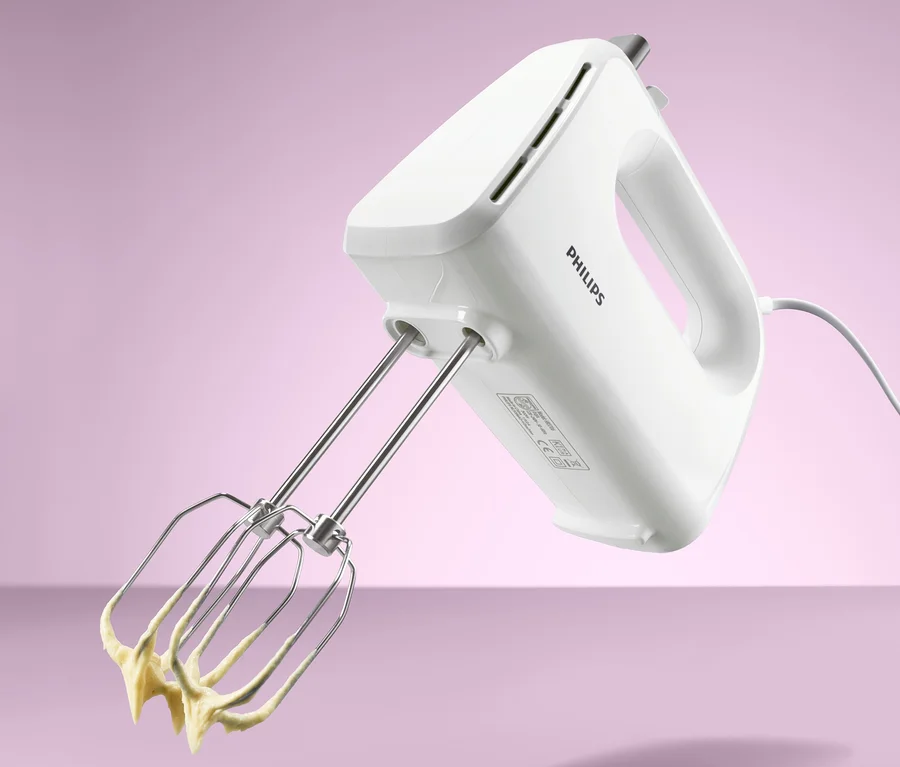 Bílý ruční mixér Philips HR 3706 s nerezovými metlami, na kterých je žluté těsto.