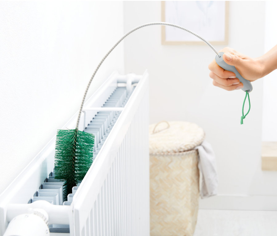 Ruka čistí radiátor kartáčem na radiátory.