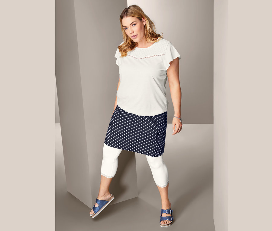 Žena pózuje v tričku s ažurovou výšivkou, proužkované žerzejové sukni a 3/4 legínách s krajkovým lemem.