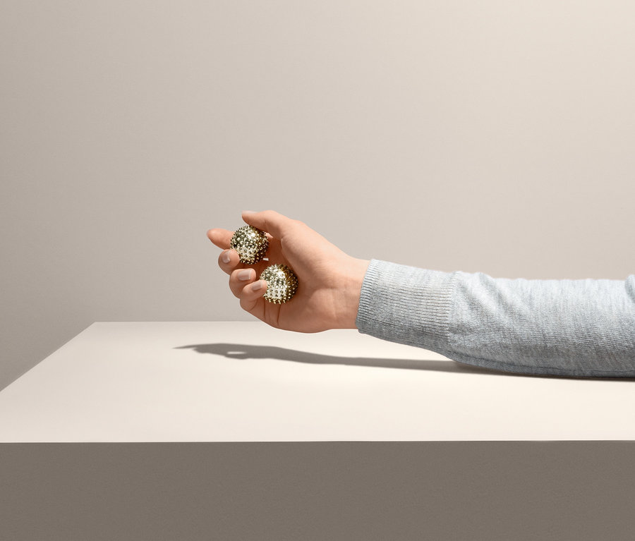 Ruka drží dva Kuličky na prstovou gymnastiku nad stolem.