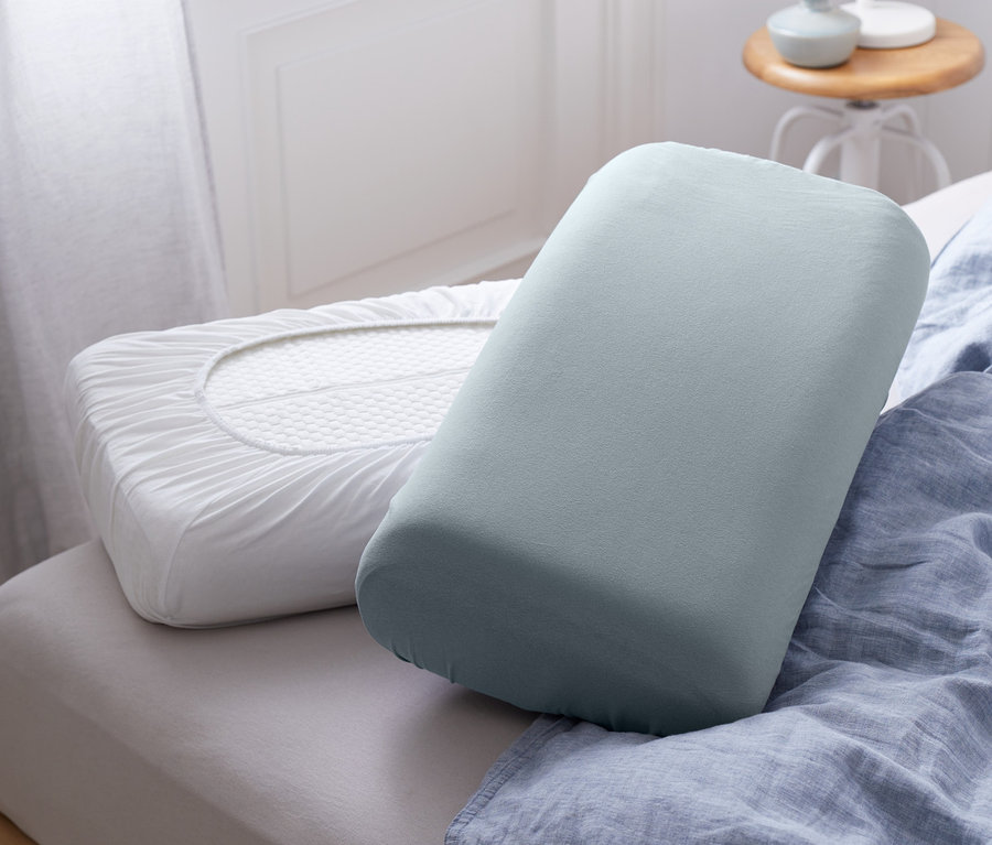 Dva žerzejové napínací povlaky na polštáře leží na posteli s modrým povlečením.