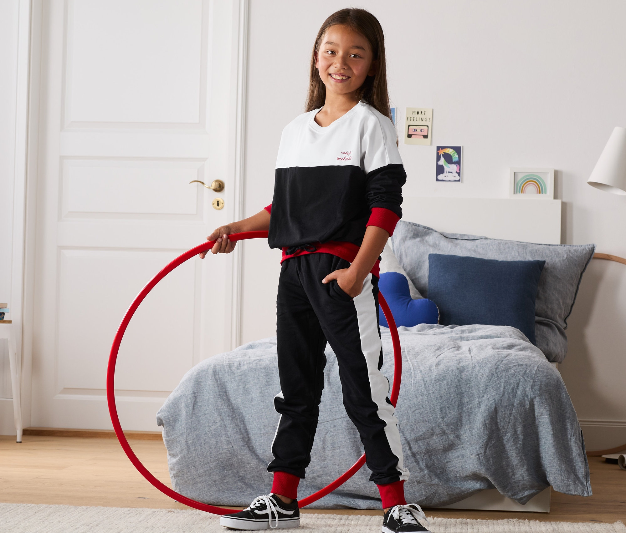 Dívka drží červenou obruč v ruce, oblečená do 2dílné teplákové soupravy.