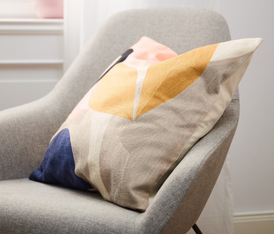 Na šedém křesle leží povlak na dekorační polštářek s geometrickým vzorem.