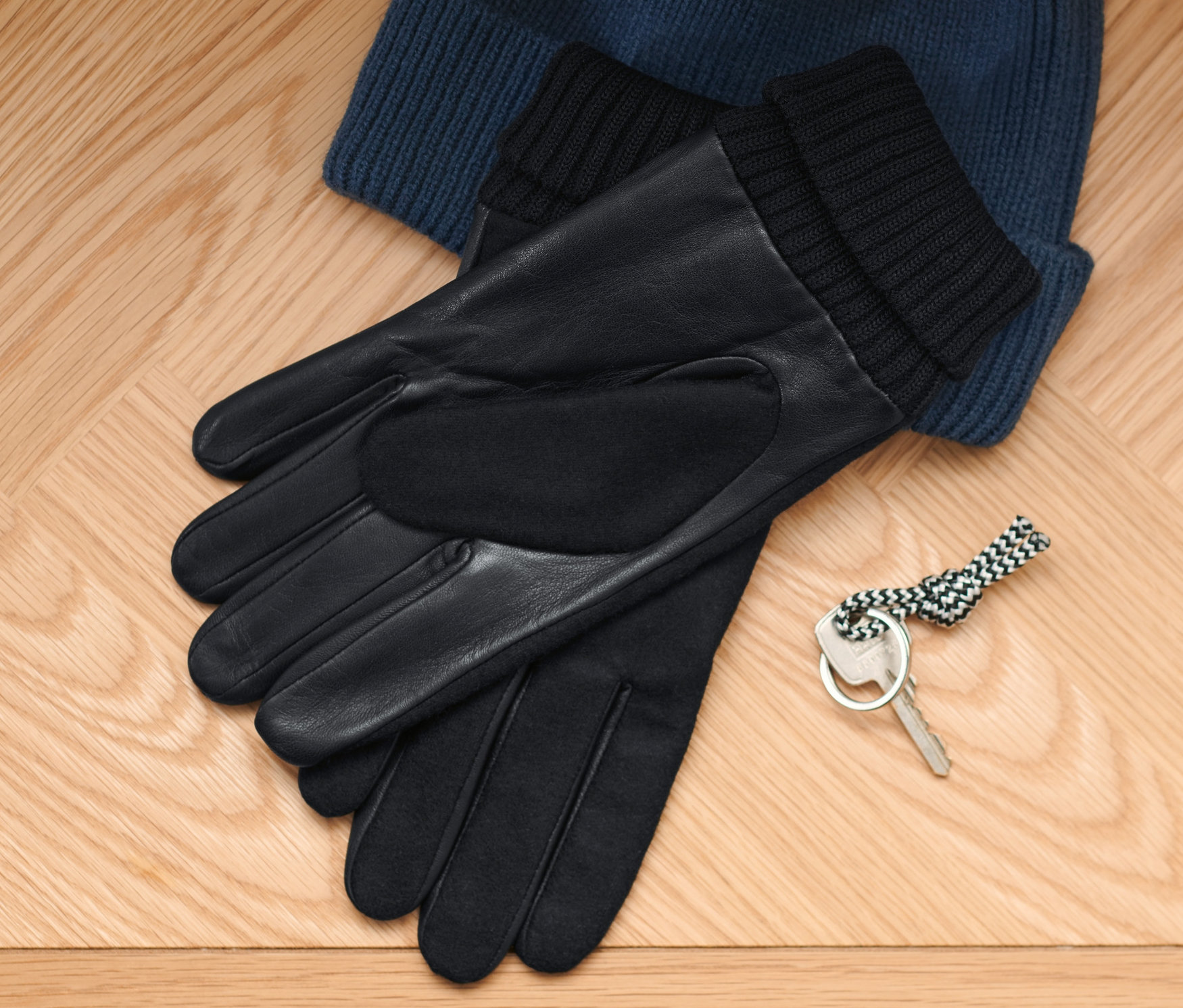 Na dřevěné podlaze leží modrá pletená čepice, černé kožené rukavice a klíč.