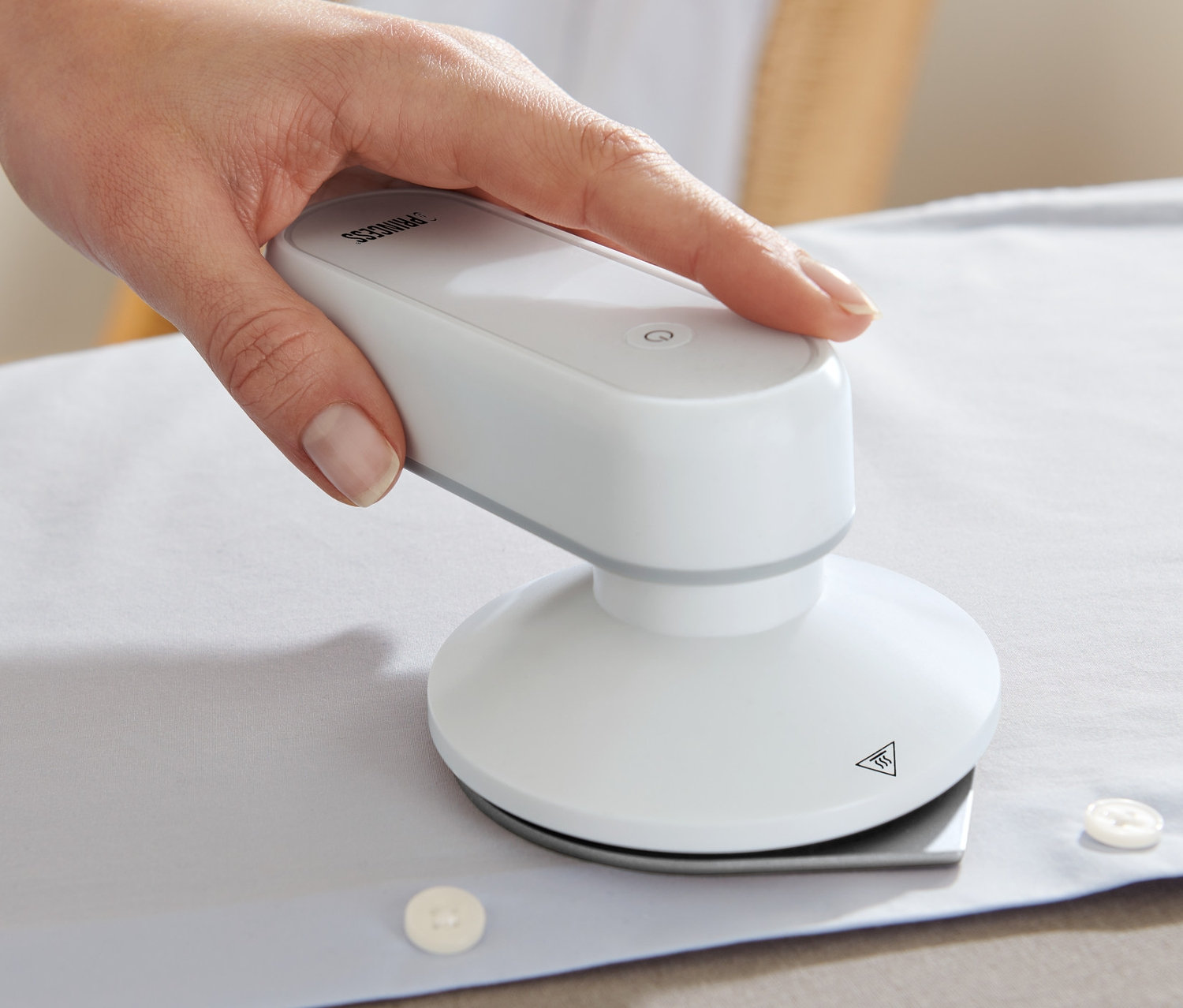 Ruka žehlí bílou košili s cestovní žehličkou Princess s powerbankou.