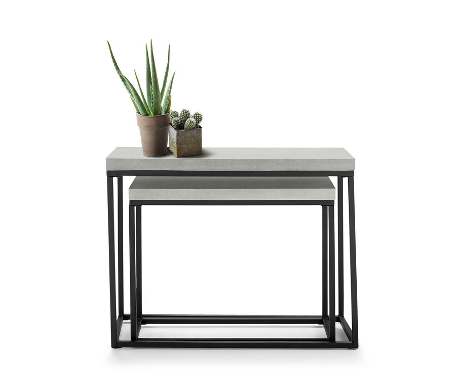 Dva konzolové stolky s betonovými deskami, jeden umístěný pod druhým. Na horním stolku stojí aloe vera a malý kaktus v květináčích.