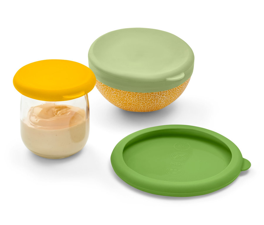 Sklenice s oranžovou tekutinou je uzavřena žlutým silikonovým víčkem. Vedle leží zelené silikonové víčko a melounová miska se zeleným silikonovým víčkem. Všechny tři položky jsou ze sady silikonových víček pro uchování čerstvosti.