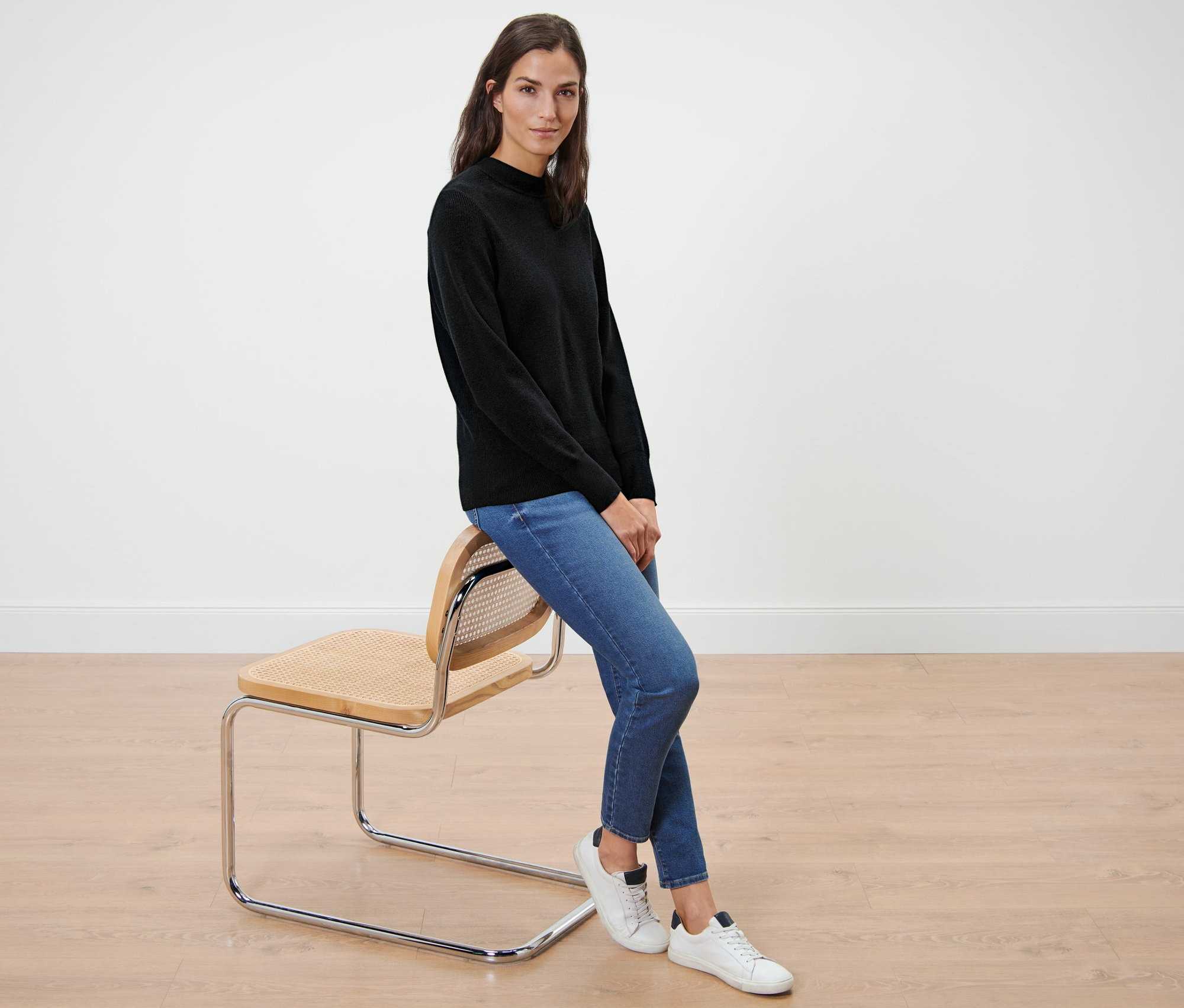 Žena sedí na židli a má na sobě černý svetr z jemného úpletu.