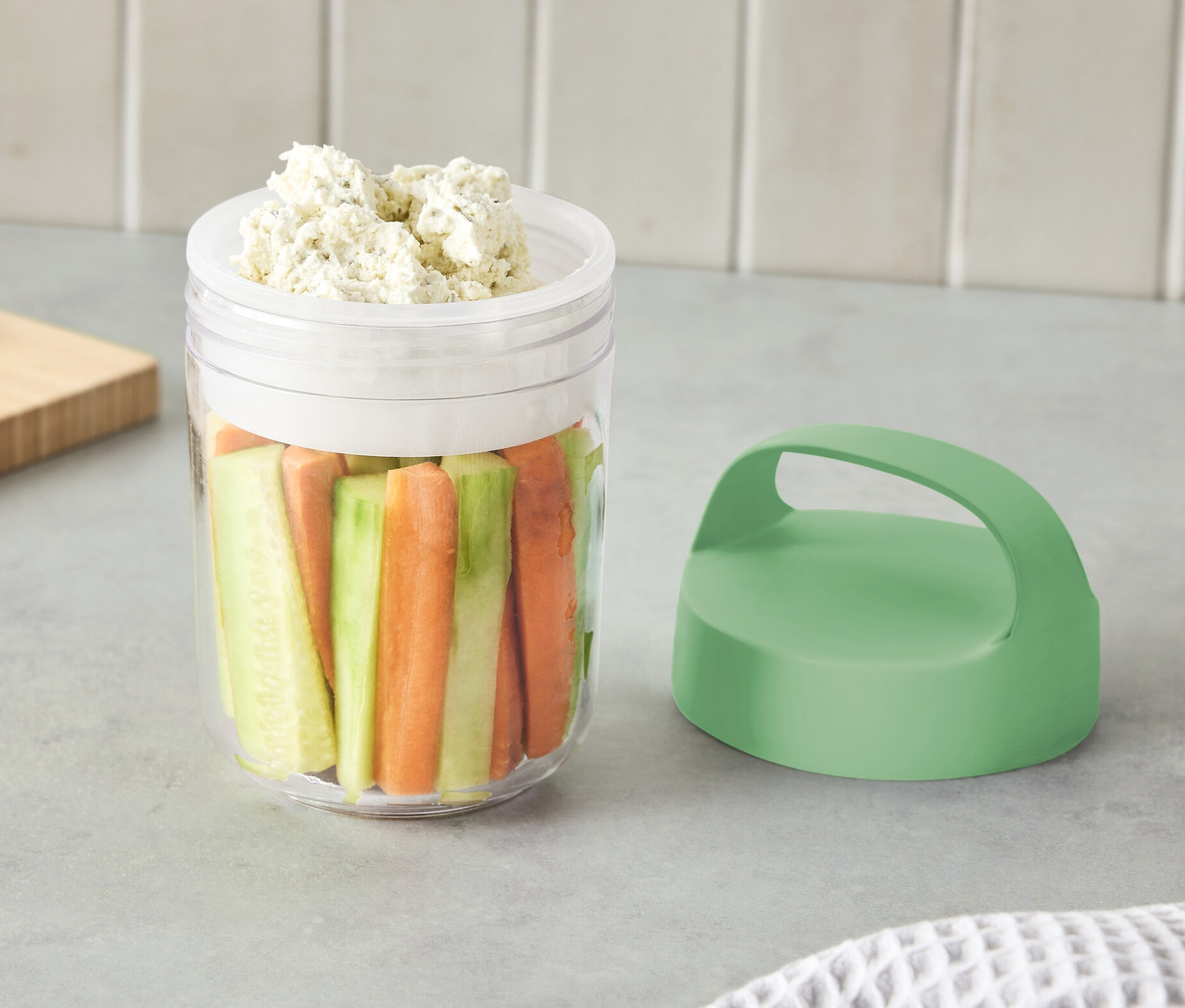 Malá cestovní nádoba s uchem plná nakrájené zeleniny a dipu.