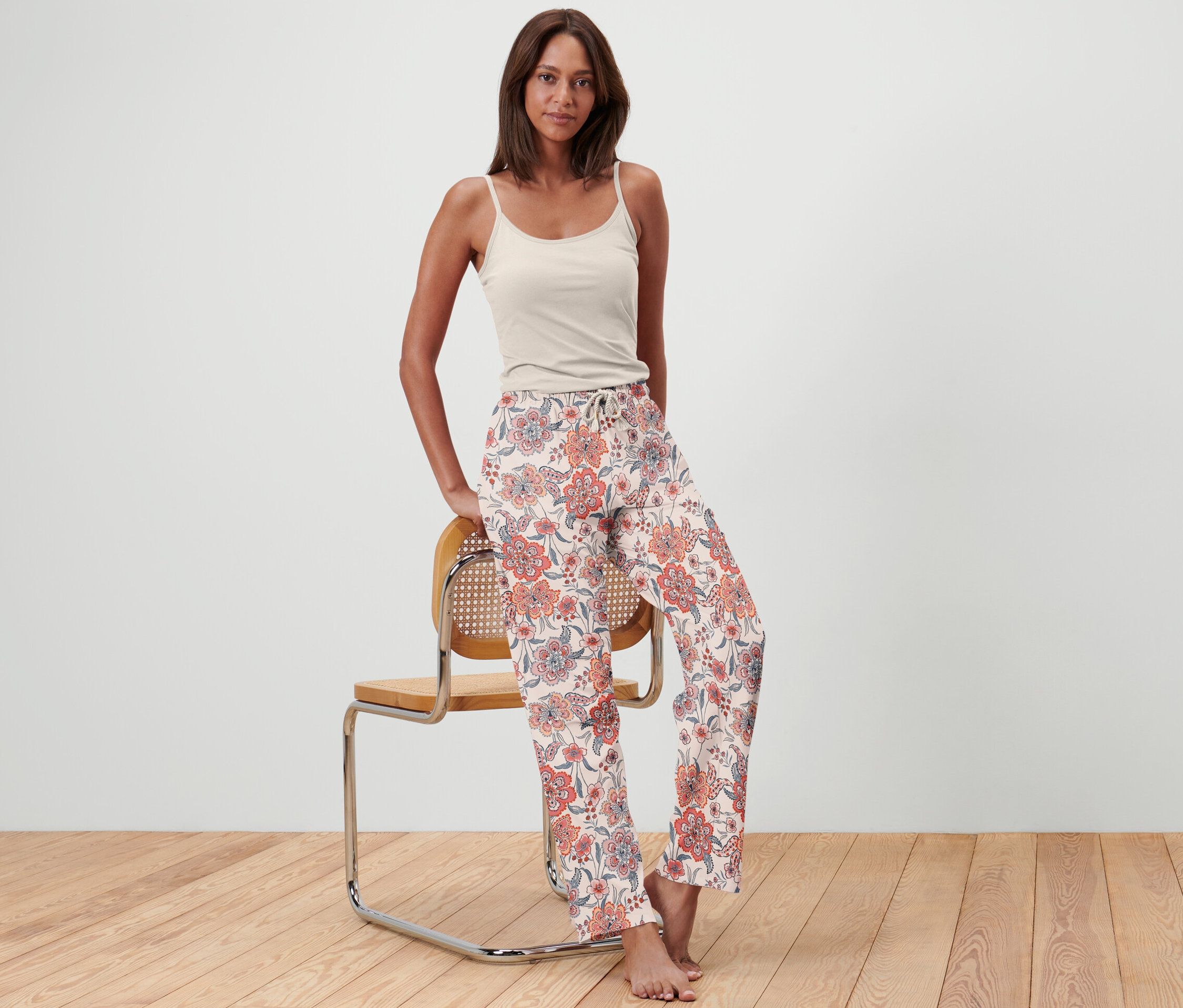 Žena stojí a opírá se o židli a má na sobě pyžamové kalhoty.