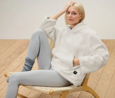 Blonďatá žena sedí na židli a má na sobě vyhřívaný svetr na baterie.