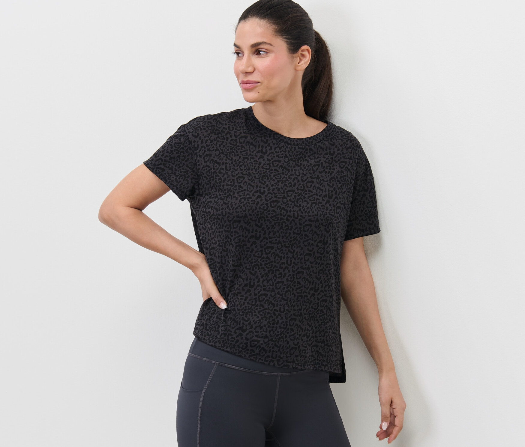 Žena pózuje v antracitovém sportovním tričku.
