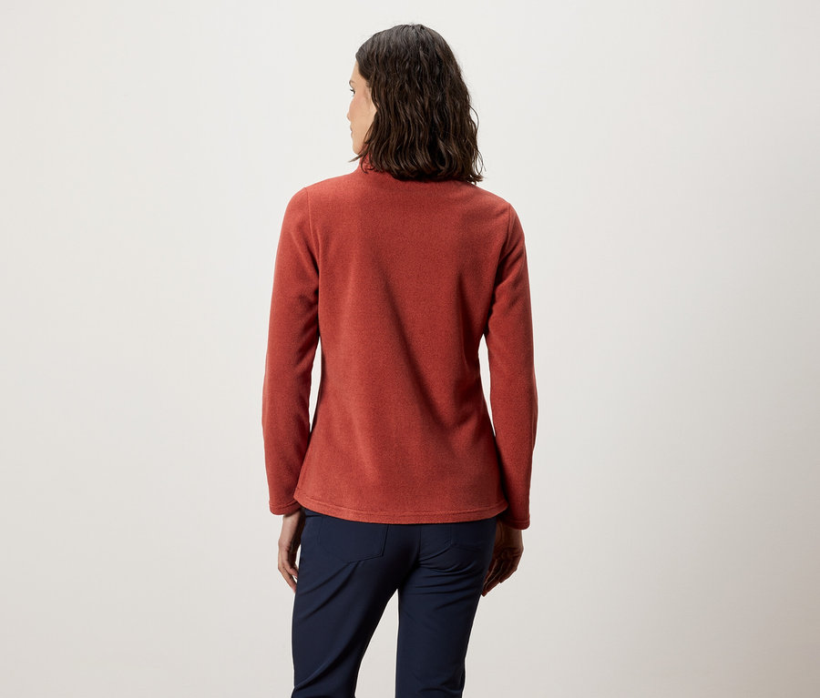 Žena zády k fotoaparátu má na sobě oranžovou fleecovou mikinu a tmavě modré kalhoty.